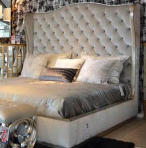 a traditional bed with the tufted headboard in a light gray fabric with a latte finished trim