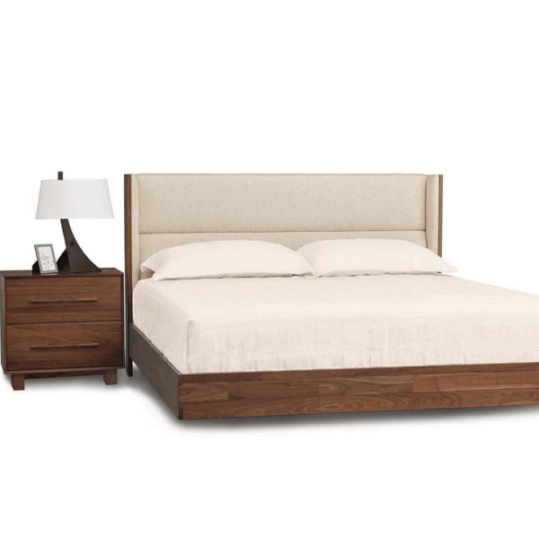 Modern floating walnut platform bed with upholstered headboard in a cream fabric and two drawer nighstand.